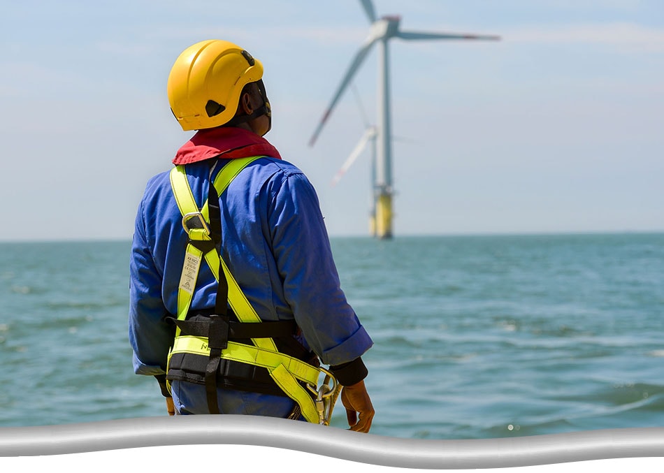 Closeup of an offshore wind turbine technician, in fully safety gear, heading towards a wind turbine in the distance.