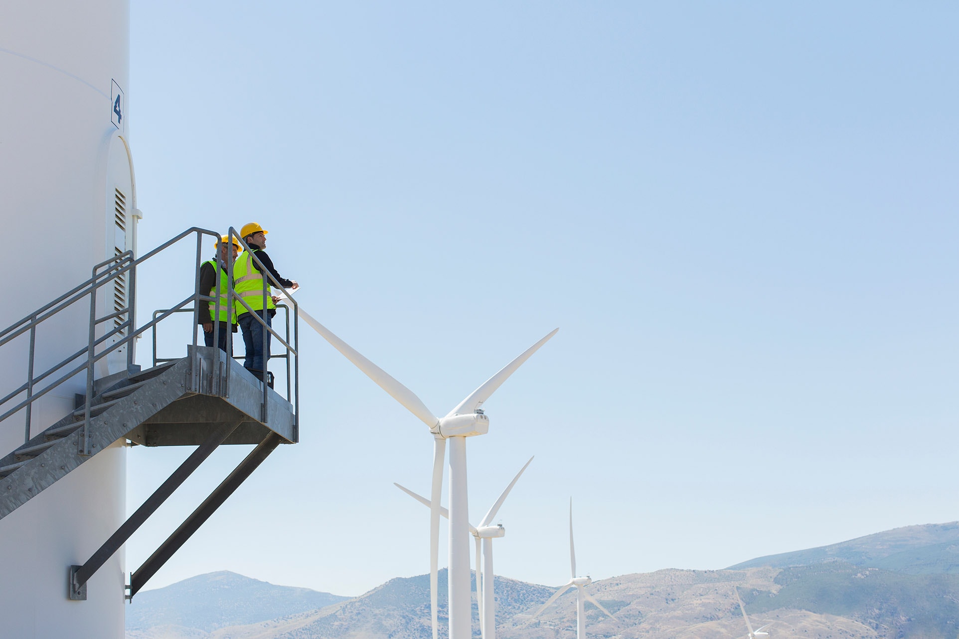 Workers standing on wind turbine in rural landscape studying the landscape and safely planning the next stages of the project